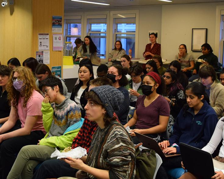 People seated and standing listening to a speaker.